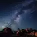 Chuva de meteoros Orionídeas iluminando o céu estrelado com a Via Láctea ao fundo em um cenário rochoso.
