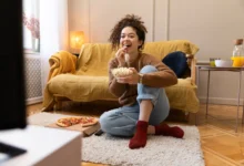 Mulher sorridente assistindo TV enquanto come pipoca, representando momentos relaxantes inspirados por novelas turcas.