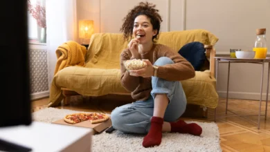 Mulher sorridente assistindo TV enquanto come pipoca, representando momentos relaxantes inspirados por novelas turcas.