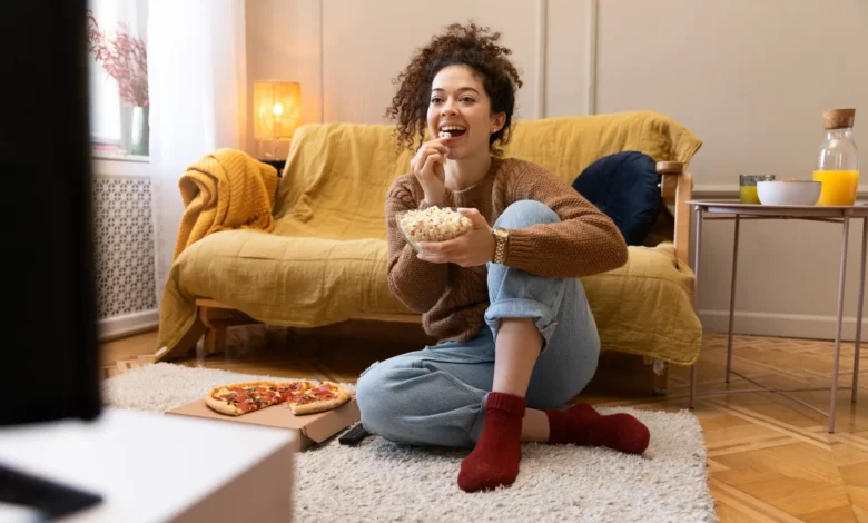 Mulher sorridente assistindo TV enquanto come pipoca, representando momentos relaxantes inspirados por novelas turcas.