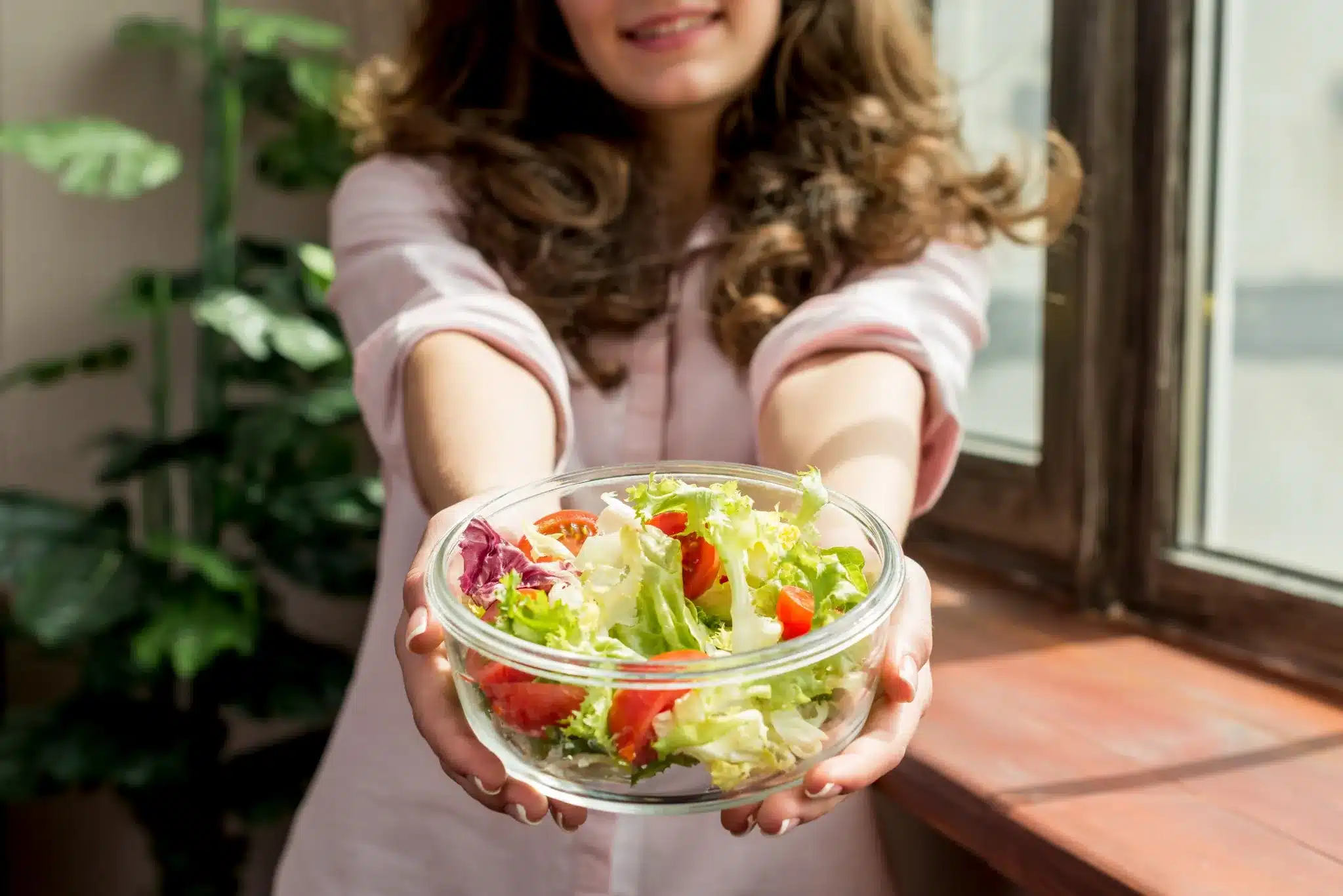 Mulher sorridente oferecendo uma tigela de salada fresca, representando uma alimentação saudável para o bem-estar do coração.
