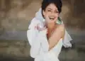 Noiva sorrindo com vestido branco e acessórios elegantes, destacando-se com brincos grandes e luvas brancas.
