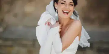 Noiva sorrindo com vestido branco e acessórios elegantes, destacando-se com brincos grandes e luvas brancas.