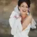 Noiva sorrindo com vestido branco e acessórios elegantes, destacando-se com brincos grandes e luvas brancas.