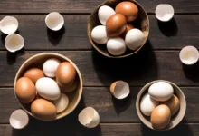 Ovos brancos e marrons em tigelas diferentes sobre uma superfície de madeira, ilustrando a comparação entre eles.