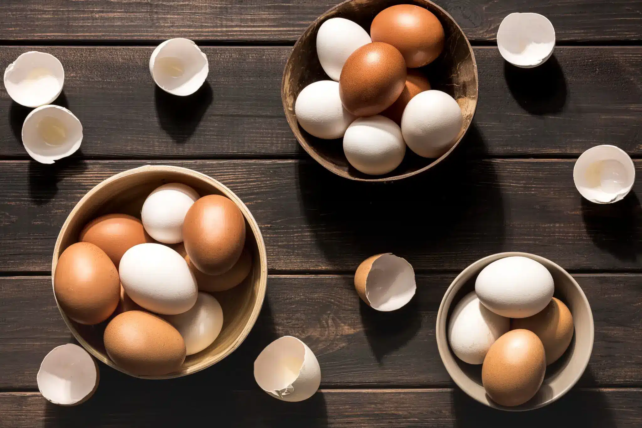Ovos brancos e marrons em tigelas diferentes sobre uma superfície de madeira, ilustrando a comparação entre eles.