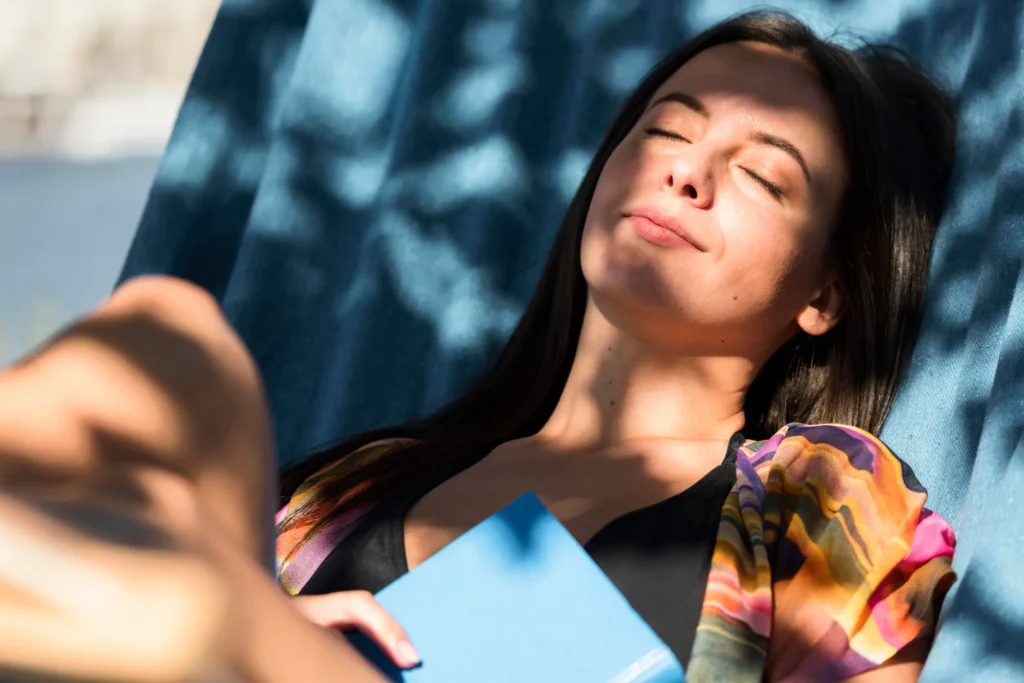 Mulher relaxando ao sol, com um livro na mão, aproveitando os benefícios da luz solar para o bem-estar.