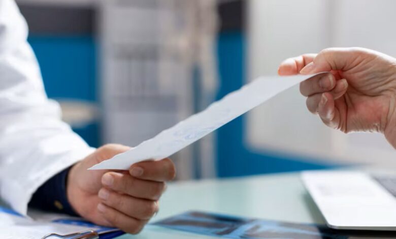 Mãos de um profissional de saúde (jaleco branco) entregando uma receita médica ou documento a um paciente. Foco na transferência da prescrição.