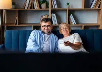 Casal sorridente assistindo novela turca na sala de estar.