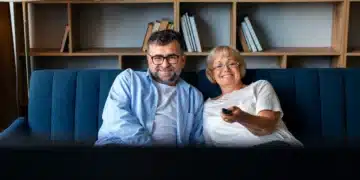 Casal sorridente assistindo novela turca na sala de estar.