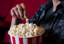 Mão pegando uma pipoca em um balde vermelho e branco no cinema, em um cenário de filme.