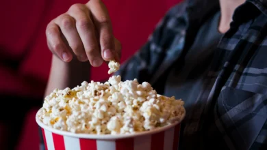 Mão pegando uma pipoca em um balde vermelho e branco no cinema, em um cenário de filme.