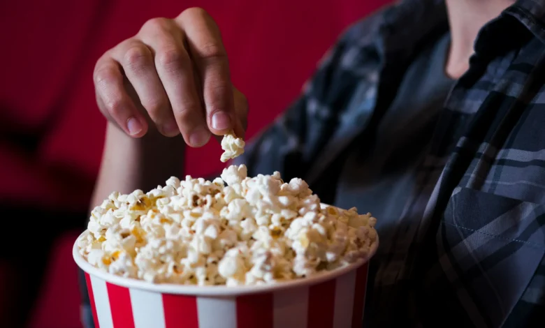 Mão pegando uma pipoca em um balde vermelho e branco no cinema, em um cenário de filme.