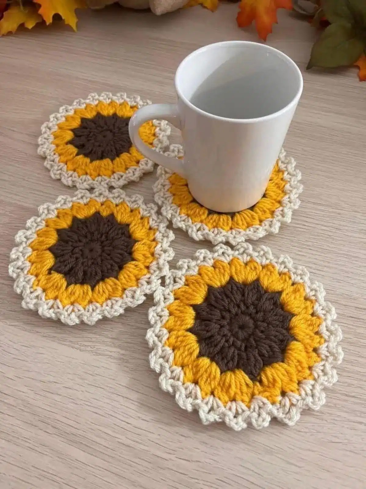 Porta-copos de crochê em formato de girassol, com cores amarelo, marrom e bege, adicionando charme à decoração.