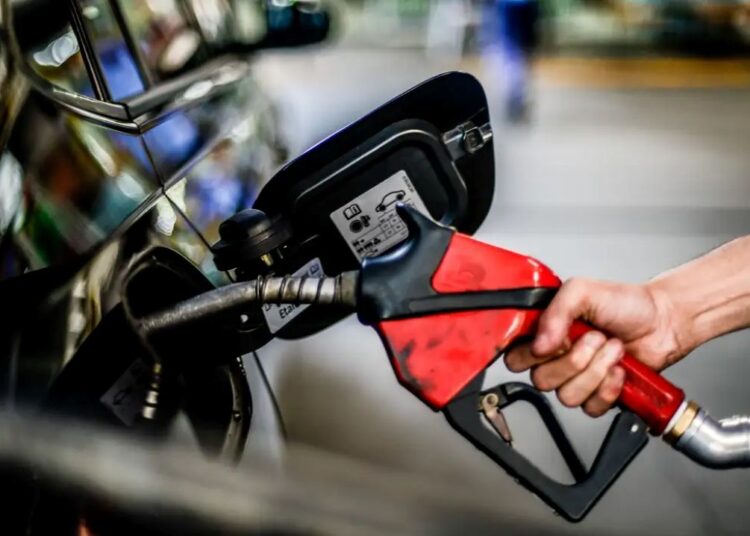 Mão segurando a bomba de combustível, abastecendo um carro, ilustrando o anúncio da Petrobras sobre o preço da gasolina.