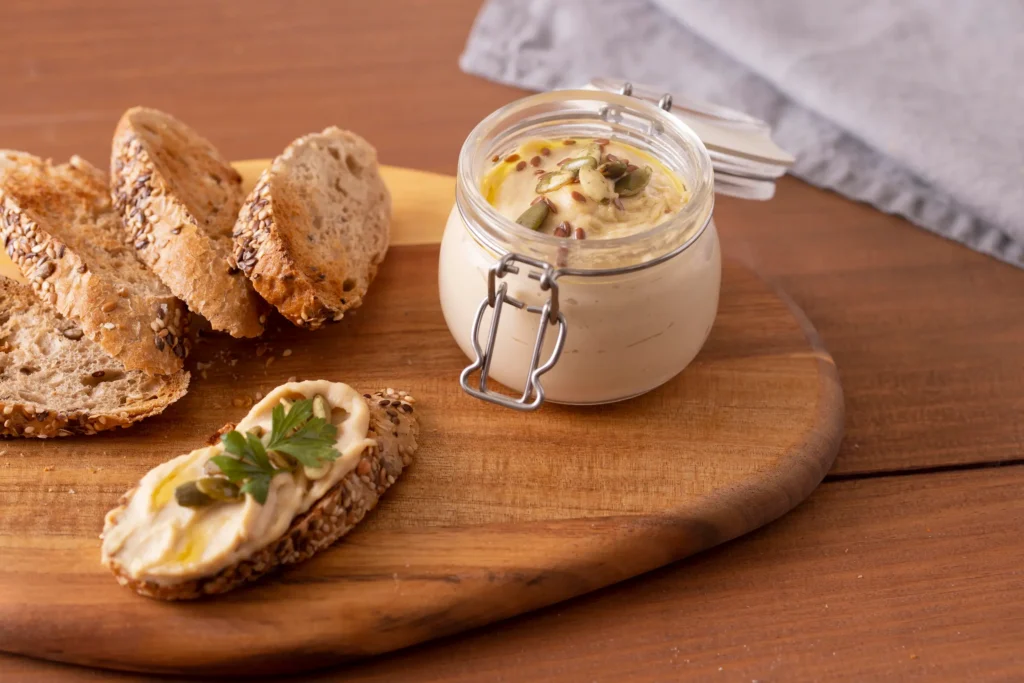 Cream cheese caseiro saudável em pote, acompanhado de fatias de pão com sementes.