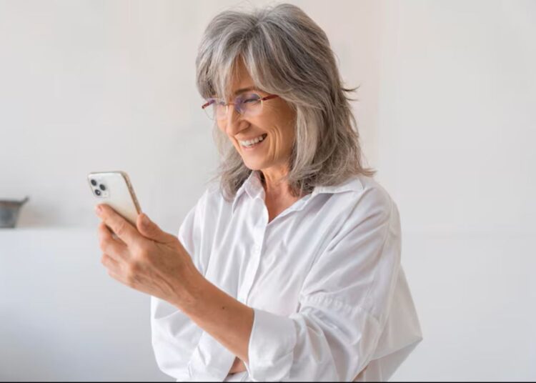 Mulher sorrindo e interagindo alegremente com um smartphone, demonstrando facilidade e satisfação ao usar o aparelho.