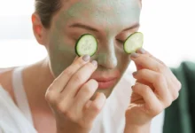 Mulher aplicando pepino sobre os olhos enquanto usa máscara facial de argila, ilustrando cuidados com a pele.