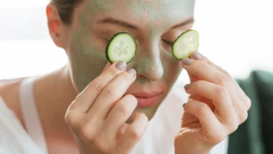 Mulher aplicando pepino sobre os olhos enquanto usa máscara facial de argila, ilustrando cuidados com a pele.