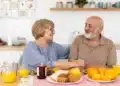 Casal sorridente tomando café da manhã saudável com frutas, suco de laranja e pães sobre a mesa.