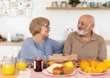 Casal sorridente tomando café da manhã saudável com frutas, suco de laranja e pães sobre a mesa.