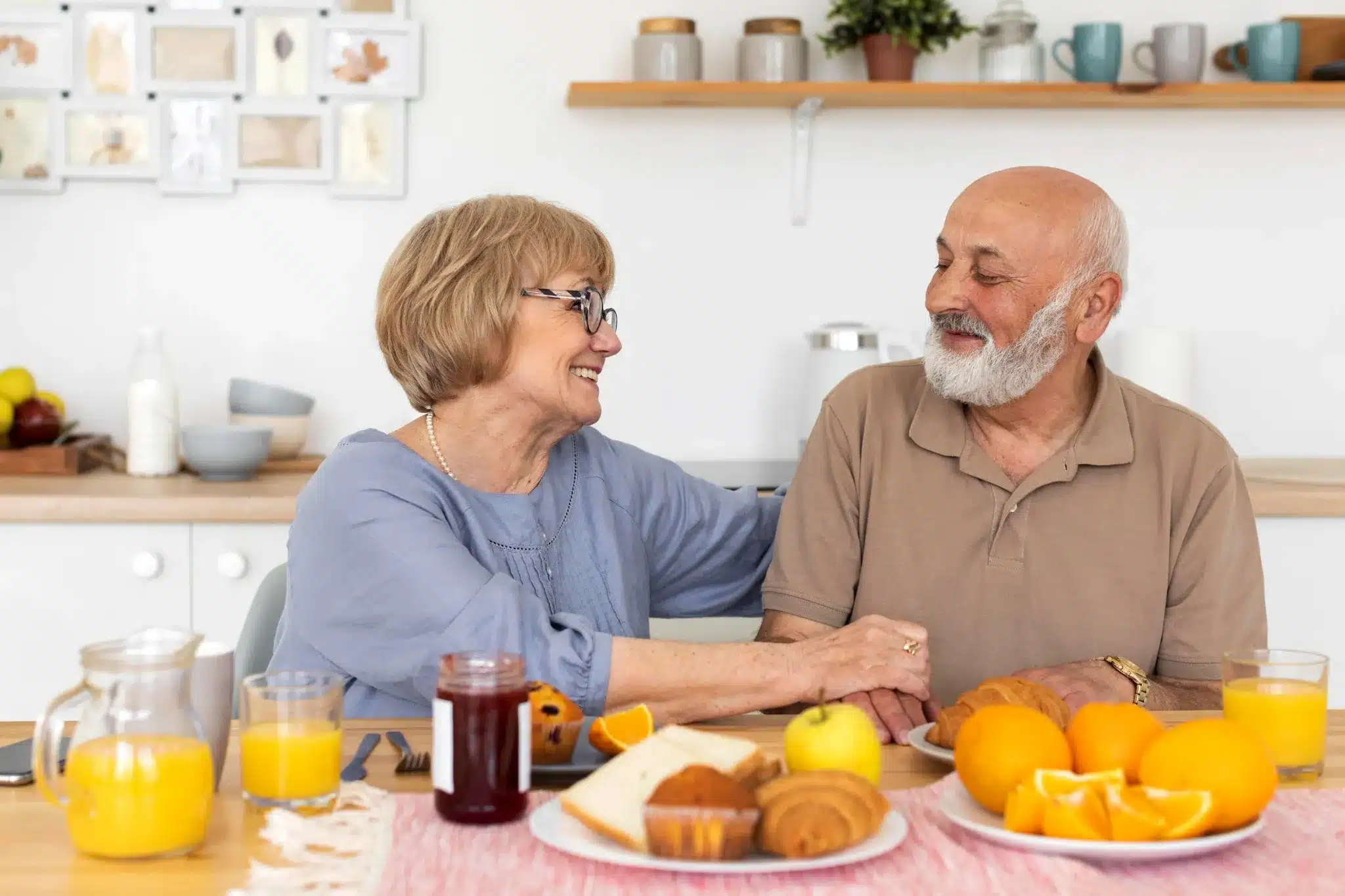 Casal sorridente tomando café da manhã saudável com frutas, suco de laranja e pães sobre a mesa.