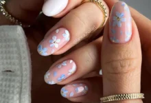 Unhas decoradas com flores delicadas em azul e branco sobre base nude — estilo de primavera elegante e moderno.