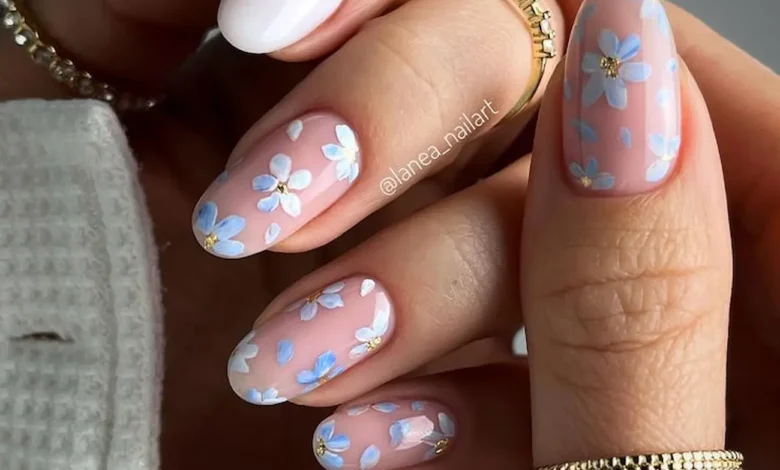 Unhas decoradas com flores delicadas em azul e branco sobre base nude — estilo de primavera elegante e moderno.