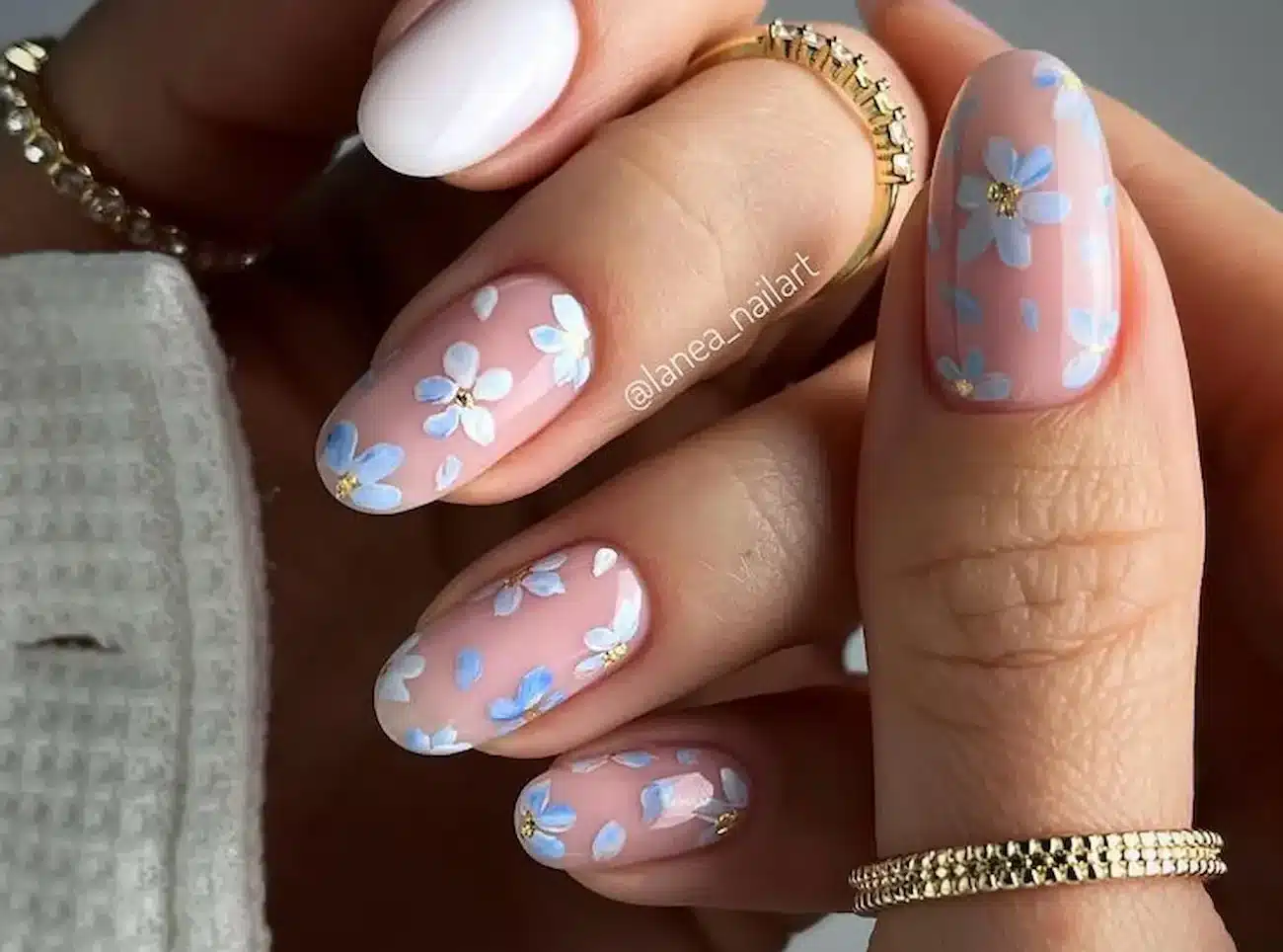 Unhas decoradas com flores delicadas em azul e branco sobre base nude — estilo de primavera elegante e moderno.