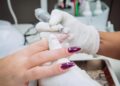 Manicure utilizando lixa elétrica para remover o alongamento de unha em gel, com profissional e cliente usando luvas de proteção em um salão de beleza.