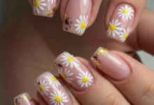 Unhas delicadas com flores brancas e amarelas, com detalhes em dourado, para a tendência de primavera de 2025.