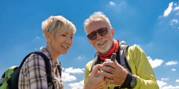 Casal de idosos sorrindo enquanto exploram a natureza, verificando equipamento em uma caminhada ao ar livre em um destino de viagem tranquilo.