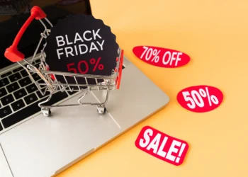 Carrinho de compras sobre um notebook com anúncios de descontos da Black Friday 2025.