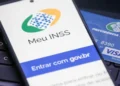 Celular exibindo tela do app Meu INSS com cartão da Previdência Social sobre teclado.