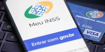 Celular exibindo tela do app Meu INSS com cartão da Previdência Social sobre teclado.