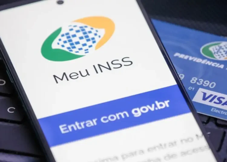 Celular exibindo tela do app Meu INSS com cartão da Previdência Social sobre teclado.
