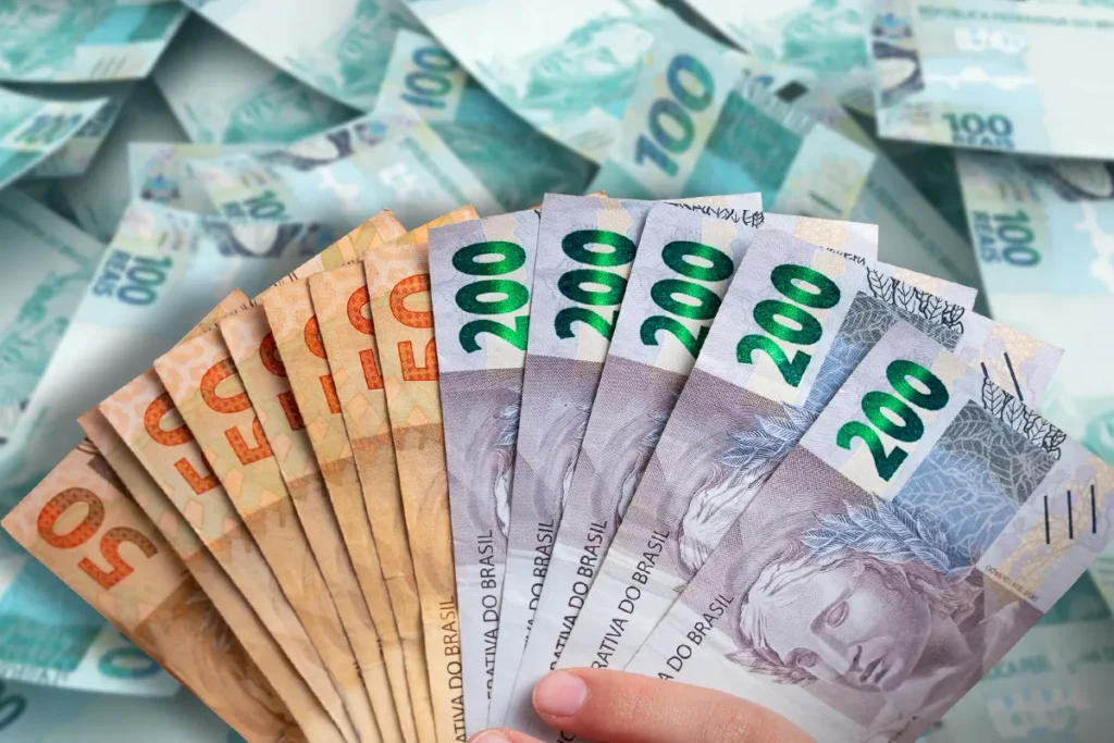 Notas de reais brasileiros, com destaque para os valores de R$50, R$100 e R$200, simbolizando auxílio financeiro.