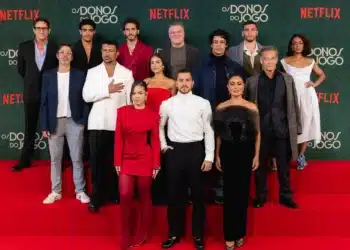 Elenco da série 'Os Donos do Jogo' posa para foto na estreia na Netflix, com trajes sofisticados, em evento de lançamento.