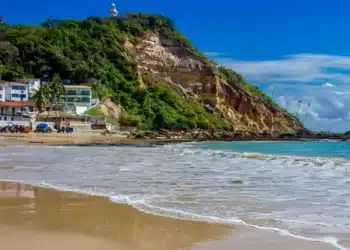 Vista paradisíaca de praia na Bahia com falésia, mar azul e casas à beira-mar após aumento da taxa de entrada.