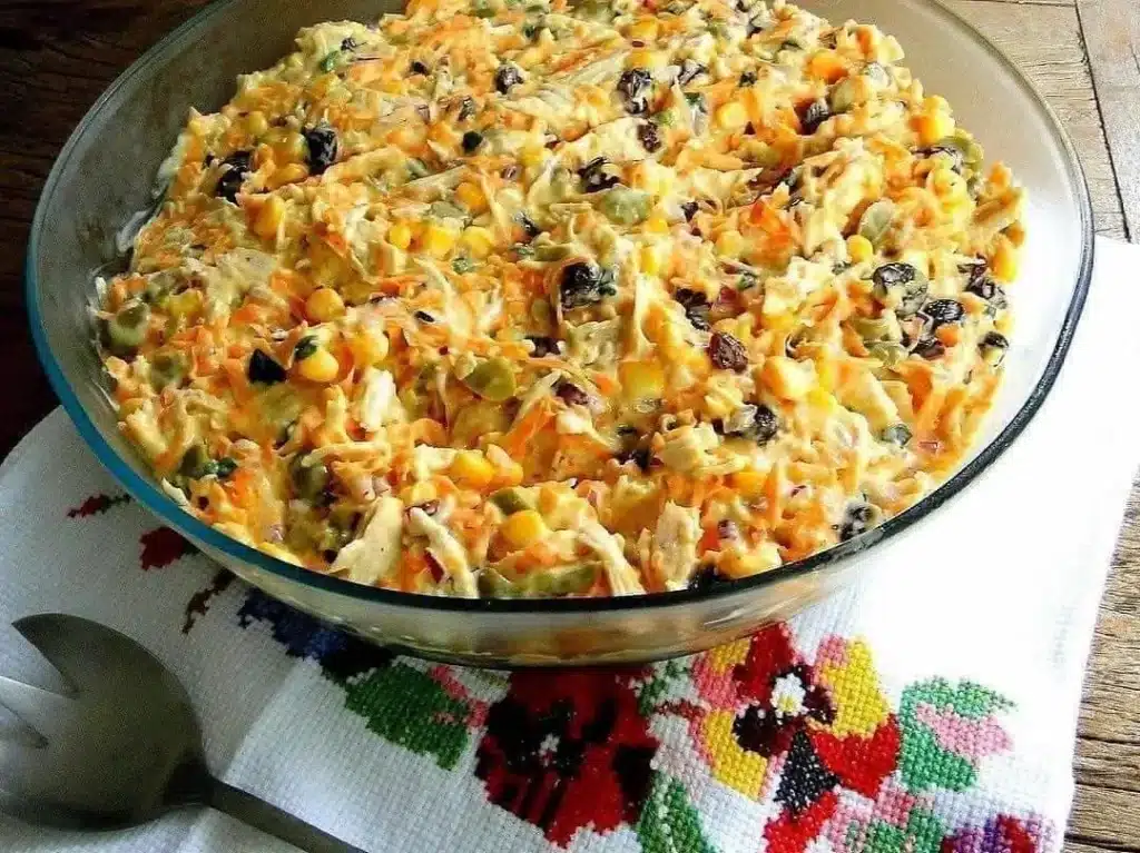 Salpicão de frango com milho, ervilha, cenoura ralada e uvas-passas, servido em uma tigela transparente.