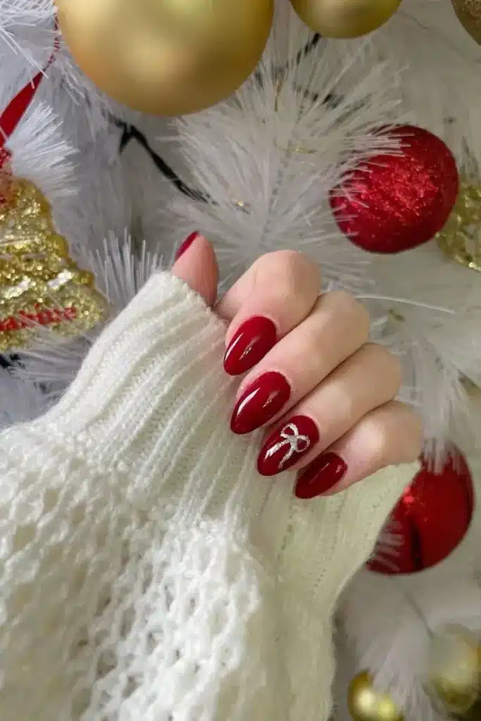 Unhas vermelhas com laços delicados de fita prateada, ideal para o Natal.