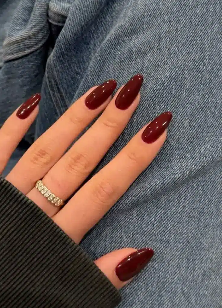 Unhas vermelhas cereja em formato amendoado com anel de diamantes visível.