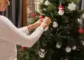 Pessoa decorando árvore de Natal com enfeites coloridos, incluindo bolinhas, flocos de neve e um boneco de neve.