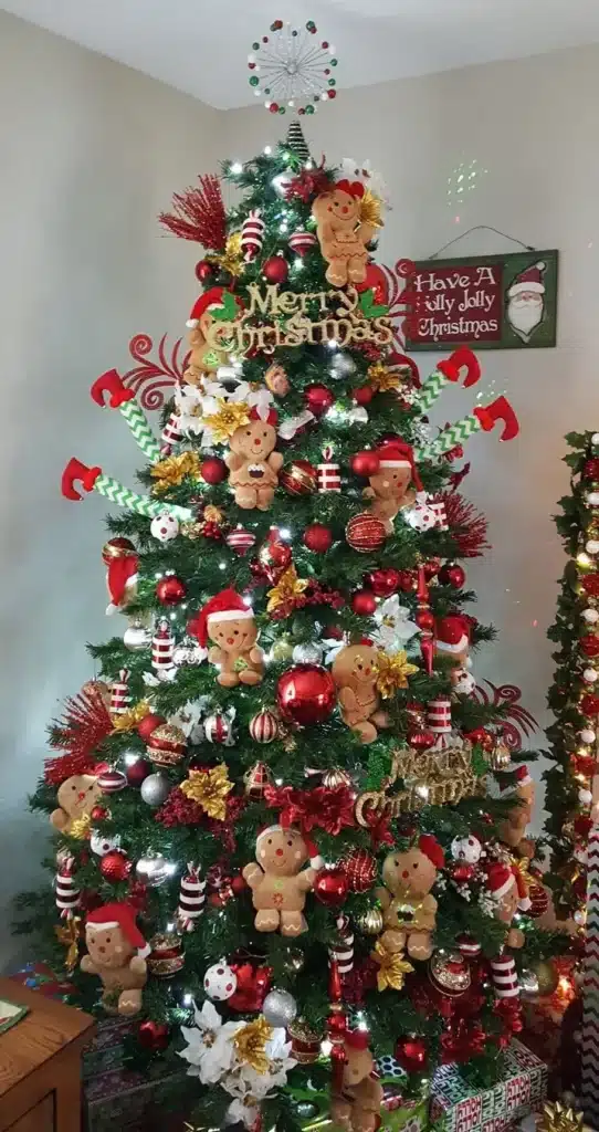Árvore de Natal com enfeites temáticos e figuras de biscoitos de gengibre. Árvore de Natal decorada com enfeites temáticos, incluindo biscoitos de gengibre, bolas vermelhas e douradas, e flores natalinas.