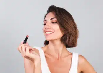 Mulher sorrindo e segurando batom, refletindo sobre tons de batom ideais para cada tipo de pele.