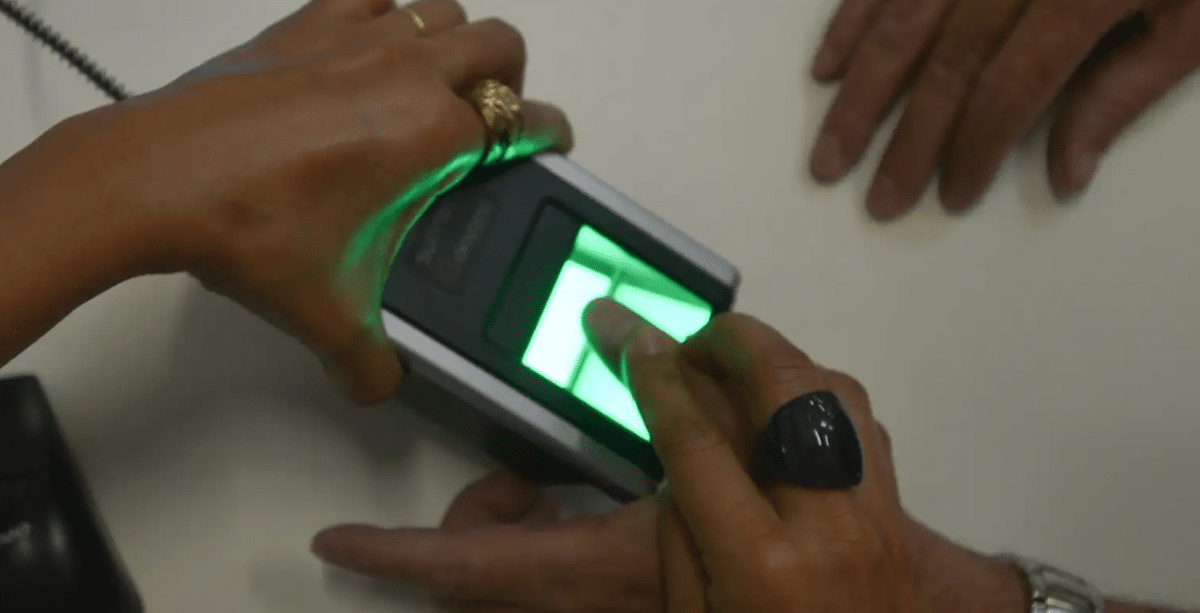 Um dispositivo de biometria com luz verde intensa, onde uma mão posiciona um dedo para leitura, ilustrando a segurança reforçada em transações financeiras e a exigência para empréstimos consignados.