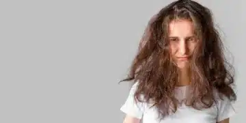 Mulher com cabelo volumoso e embaraçado, mostrando expressão de frustração, ilustrando o impacto do calor no cabelo.