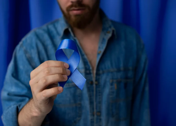 Homenagem ao Novembro Azul: Homem segurando fita azul, símbolo da luta contra o câncer de próstata, em ambiente com fundo azul.