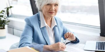 Mulher sênior sorridente em ambiente de trabalho moderno, simbolizando o sucesso na carreira após os 60 anos.