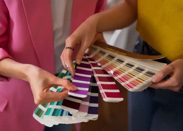 Dupla de mãos segurando diferentes amostras de cores, com foco nas paletas de tonalidades frias e quentes, para ajudar a escolher a cor ideal em casa.